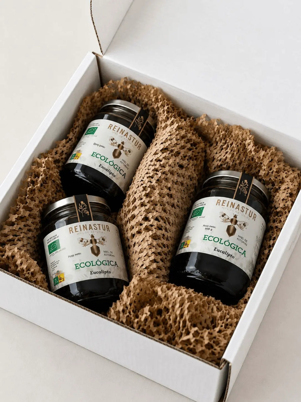 Caja de cartón blanca para regalo con tres botes grandes de miel ecológica de Eucalipto Reinastur protegidos con papel troquelado marrón.