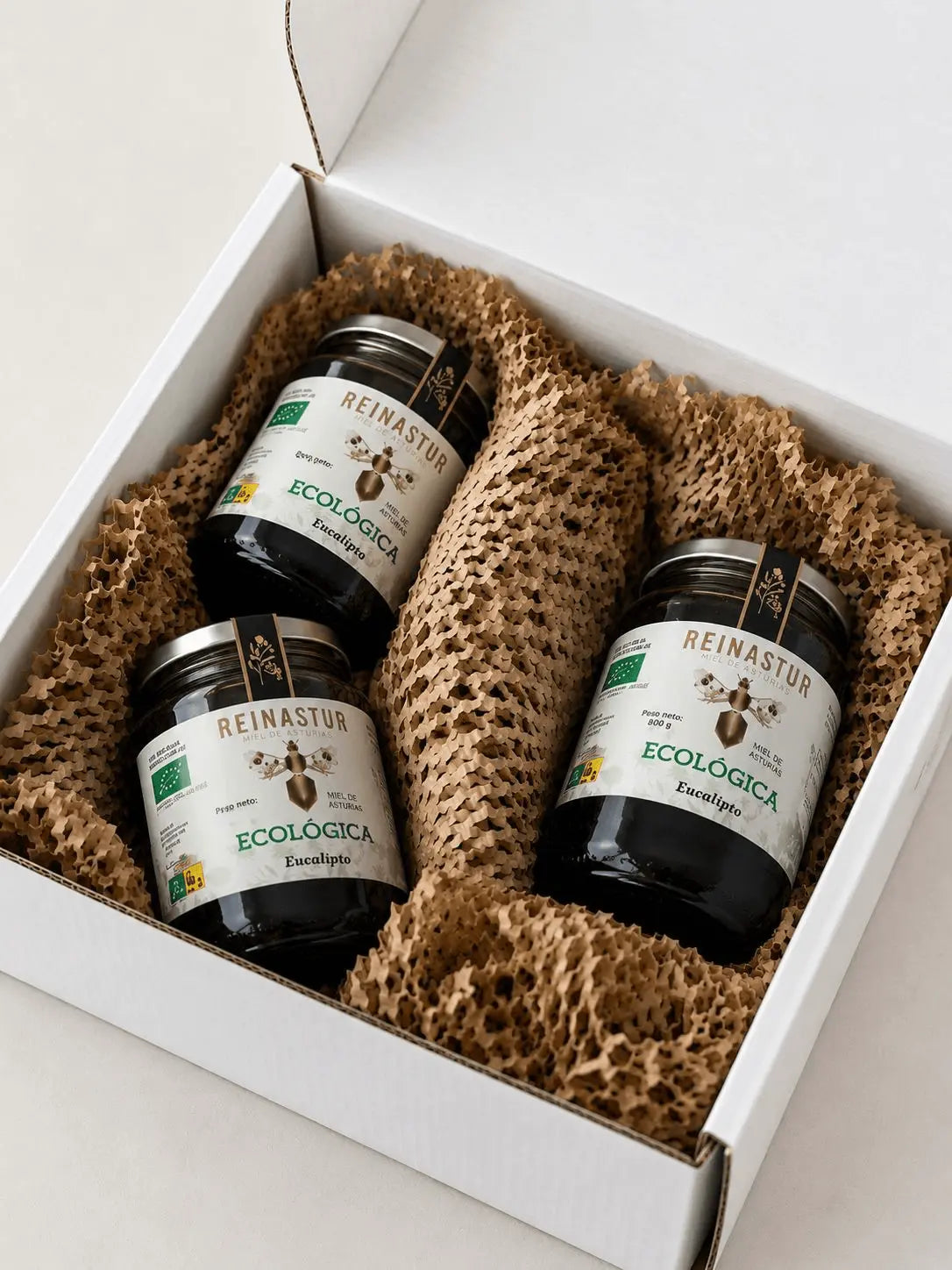 Caja de cartón blanca para regalo con tres botes grandes de miel ecológica de Eucalipto Reinastur protegidos con papel troquelado marrón.
